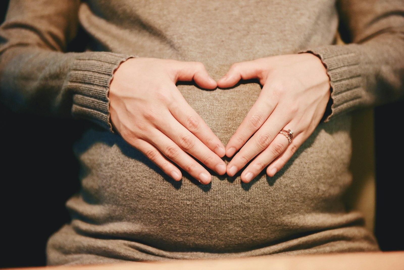 Hands forming a heart over a baby bump